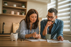 Couple reviewing paperwork and checking numbers together on a kitchen counter, focusing on household budget, financial planning, and saving money while having coffee